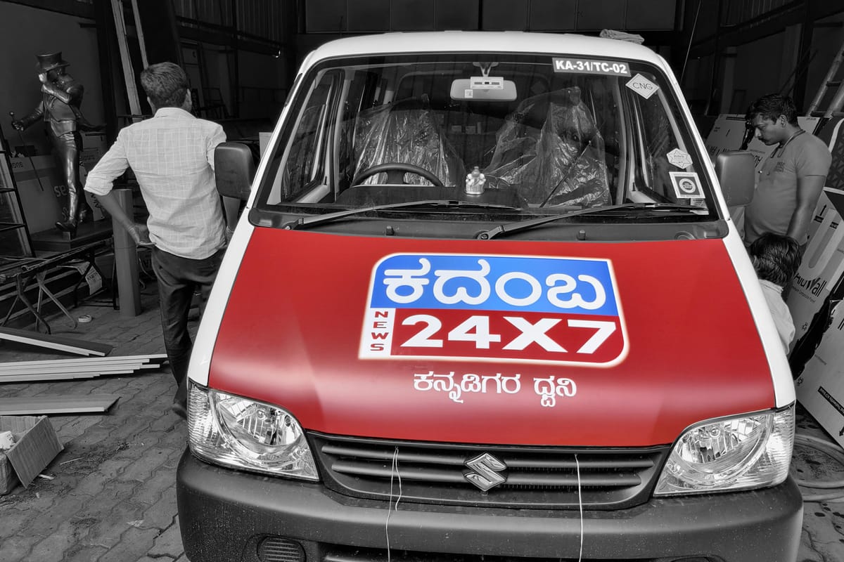 Front of a white Eeco van in a workshop, red bonnet wrap printed with the Kadamba News 24X7 logo.