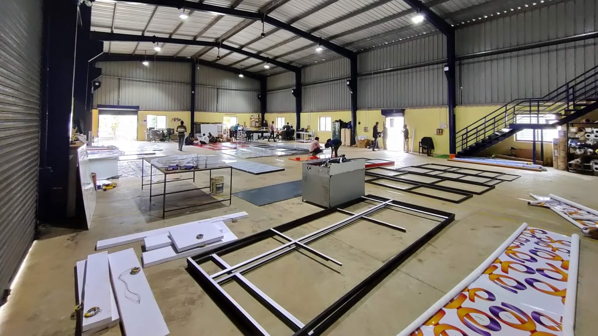 Wide view of a steel-framed fabrication hall with signage frames and panels laid out across the floor.