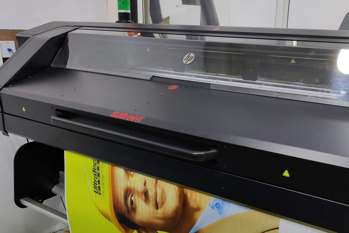Wide-format latex roll printer marked Sushant feeding out a printed cement-brand banner.
