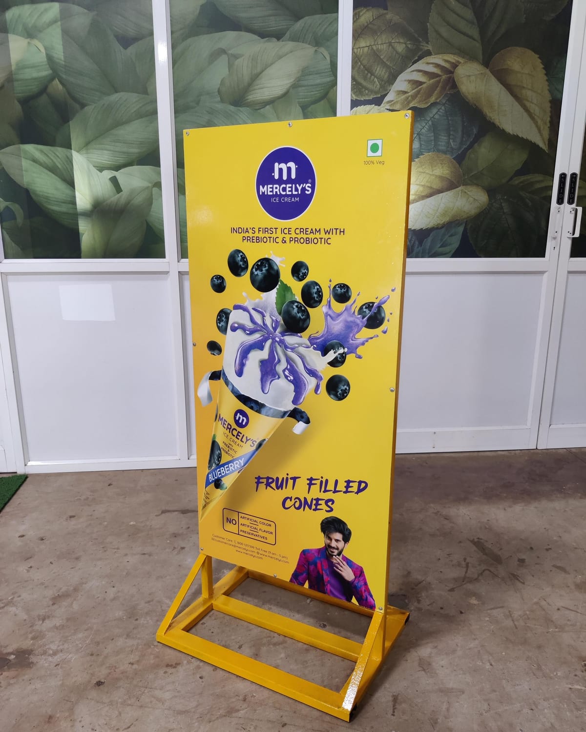 Mercely's blueberry ice cream standee on a yellow steel base in front of a glass wall with printed leaf graphics.