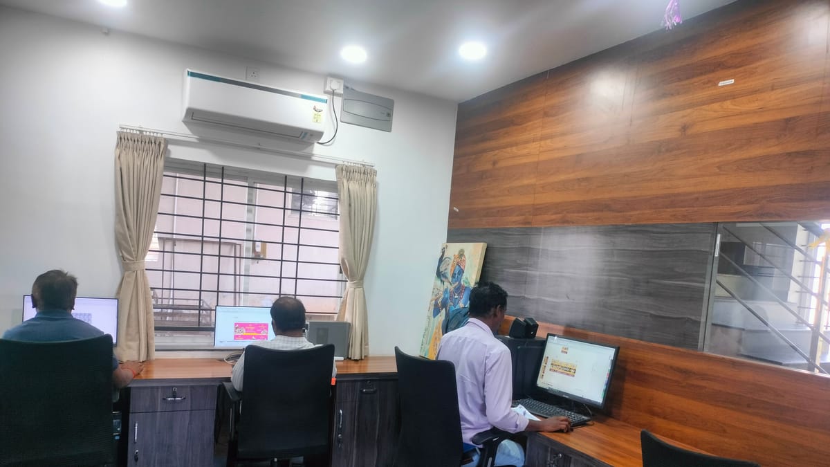 Three people working at computer workstations along a wooden counter in a design office.