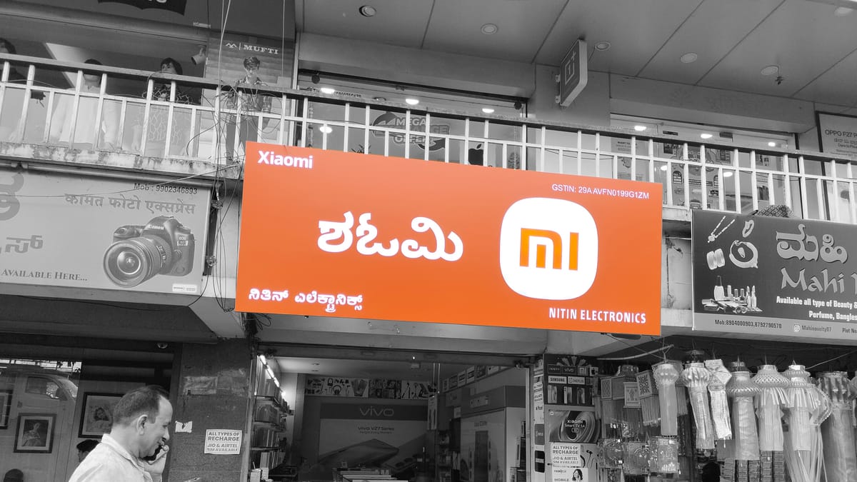 Orange Xiaomi Mi shopfront signboard with Kannada lettering above an electronics shop on a street.