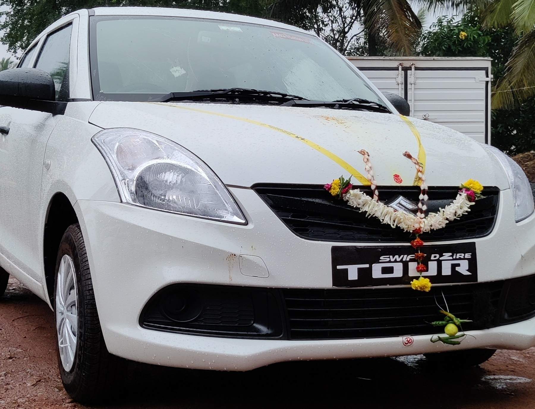 White Swift Dzire Tour with a marigold garland, ready for duty