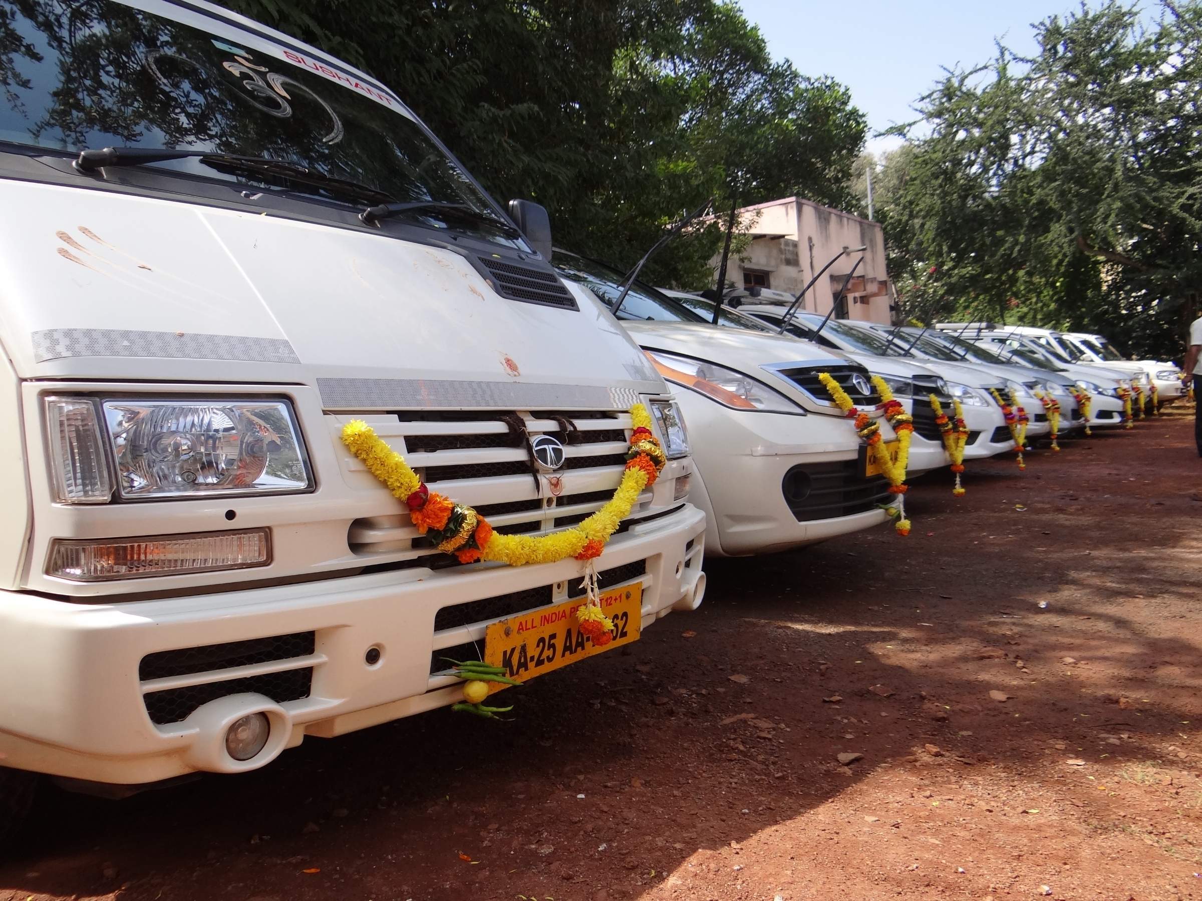 Line of white Sushant tempo travellers with garlands