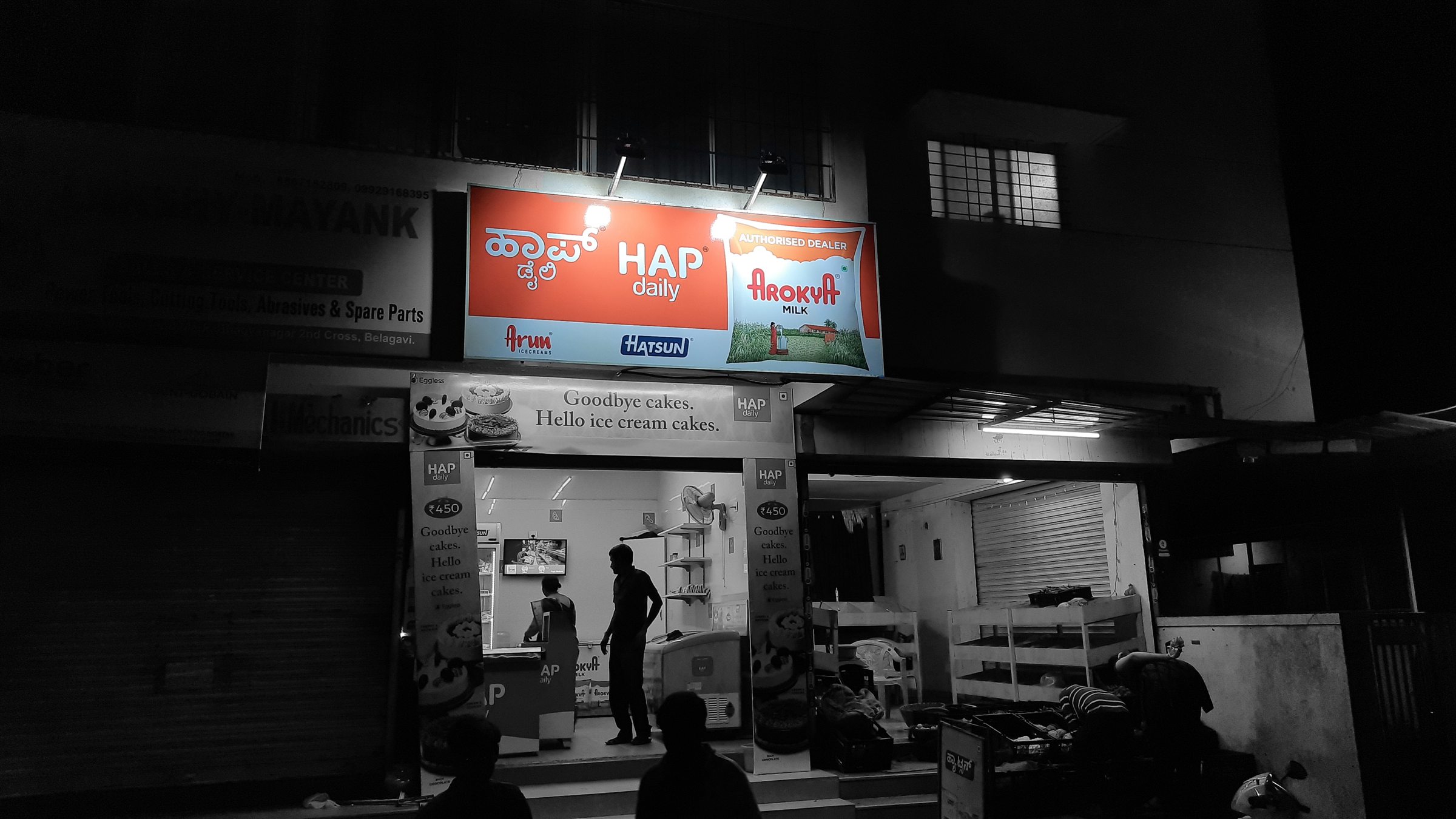 Illuminated HAP Daily dairy parlour fascia at night with Kannada and English lettering
