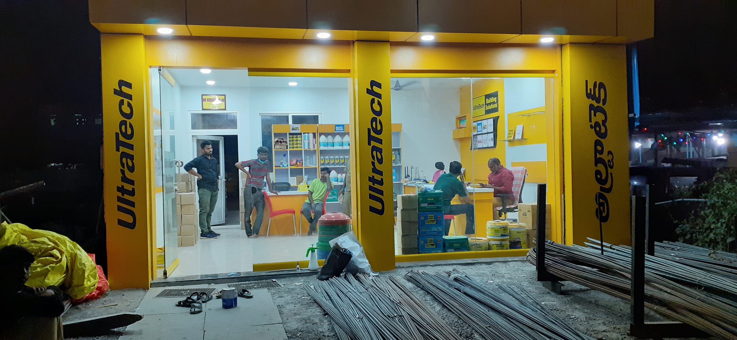 UltraTech Building Solutions store at night, with lit yellow fascia and branded pillars